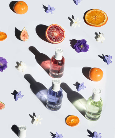 The three Evergreen scents from Modern Magic—Melted Magic, Midnight Magic, and Muse Magic—are surrounded by oranges, figs, and flowers.
