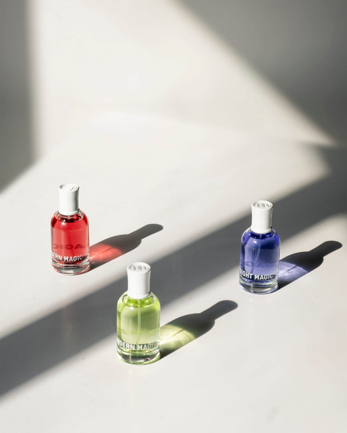 The three Evergreen scents from Modern Magic—Melted Magic, Midnight Magic, and Muse Magic—are showcased at an angle, each with a shadow cast behind it.