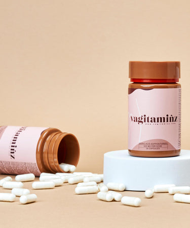 Two bottles of the best vaginal suppositories, one displayed on a round white block and the other tipped over spilling the suppositories.